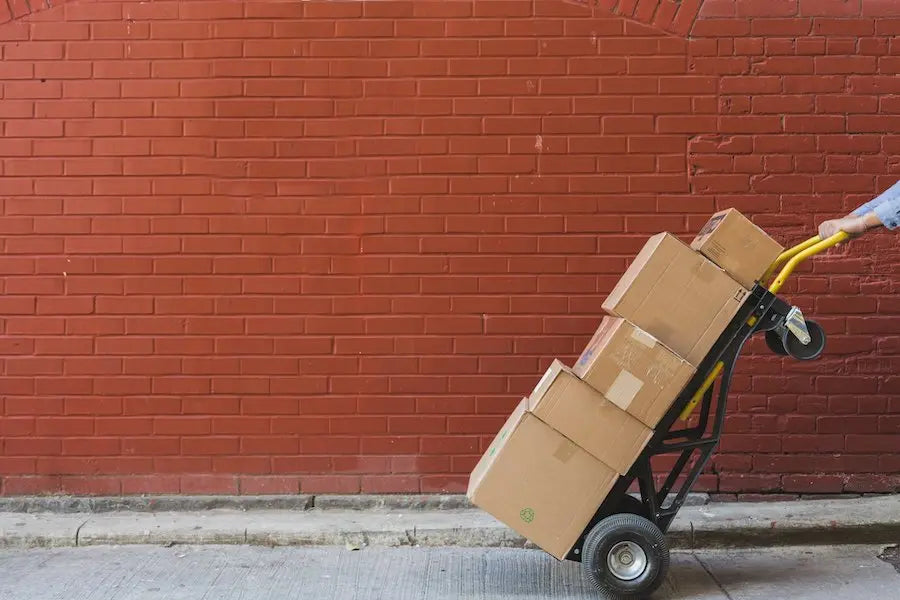 Person pushing a cart with cardboard boxes against a red brick wall.